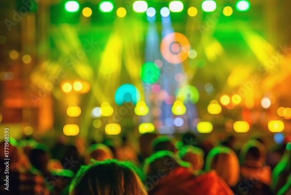 Fototapeta Blurred view of colorful concert stage with bright lights and crowd silhouettes during night event. Abstract background. Concept of music festival, party atmosphere, nightlife entertainment