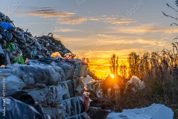 Fototapeta Sunset over a landfill showcasing garbage piles and natural beauty in the distance in late afternoon