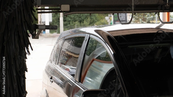 Fototapeta A dark car enters or exits an automatic car wash. The brush curtains and the upper structure of the machine are appreciated. It represents vehicle maintenance and service.