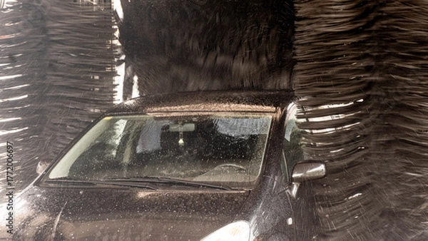 Obraz Front view of a dark car inside an automatic car wash. The large side brushes and the upper brush of the machine are visible, ready to clean the vehicle.