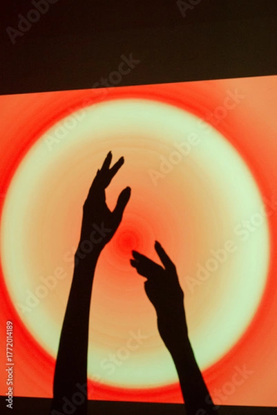 Fototapeta Hands reaching towards a glowing circle on a vibrant red and orange background during a creative event