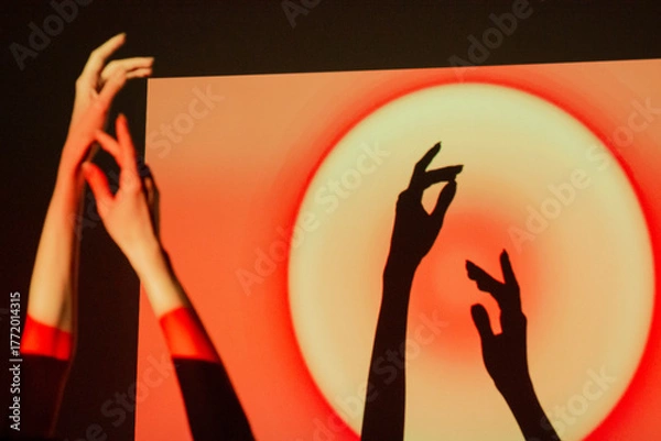 Fototapeta Shadows of hands interact with vibrant light patterns in a creative art display during the evening hours