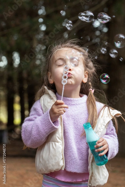 Fototapeta Child blowing bubbles outdoors in a fun playful scene