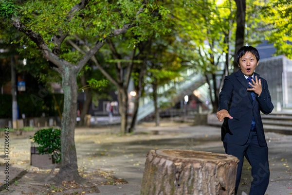 Fototapeta 大きな切り株を指さして驚くサラリーマン、夜の公園で思わず驚愕するスーツ男性