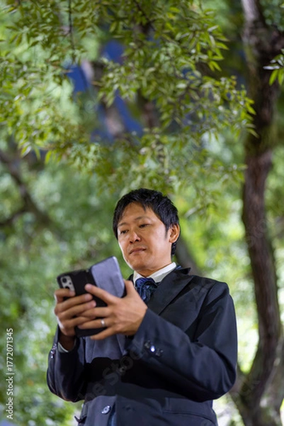 Fototapeta スマートフォンを操作するスーツの男性、夜の公園でスマホを確認するビジネスマン