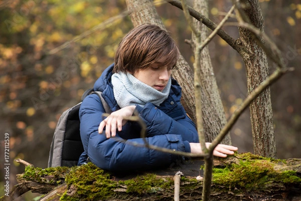 Fototapeta A 13-year-old teenage boy walks in the forest and touches the moss on a tree.