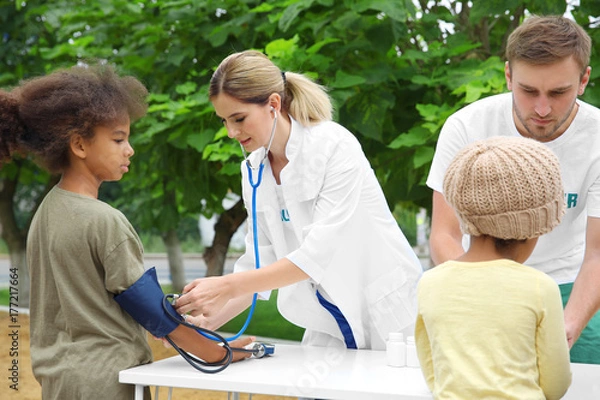 Fototapeta Volunteer doctor measuring blood pressure of poor African child outdoors