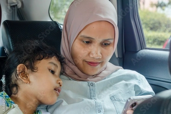 Fototapeta A muslim mother and her daughter using smartphone while traveling by car