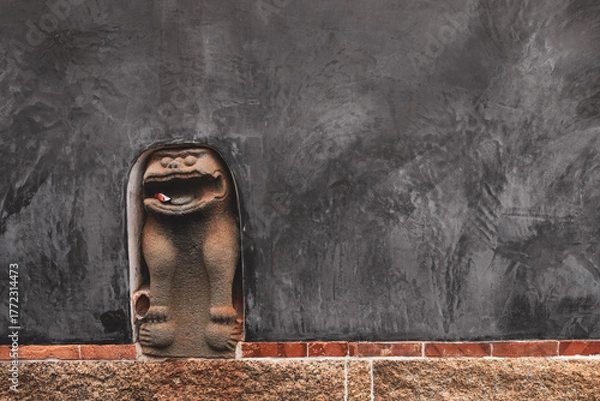 Fototapeta Wind Lion God of Kinmen embedded in wall to prevent bad luck. Copy space, grey wall background.