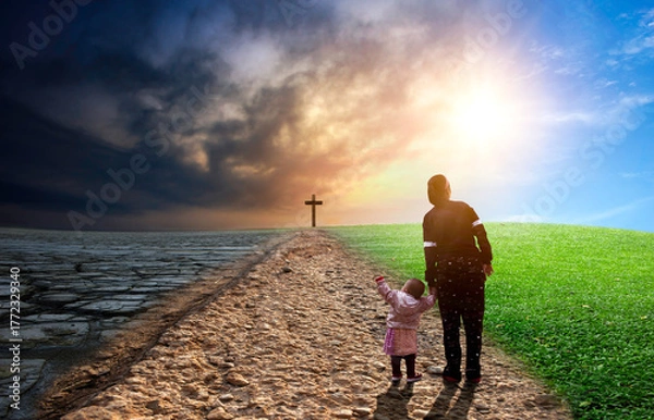 Fototapeta Silhouette of a mother and his daughter standing on a path leading to the cross