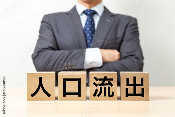 Fototapeta 「人口流出」と書かれたブロックと腕組みをするビジネスマン