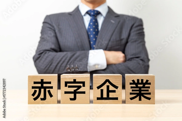 Obraz 「赤字企業」と書かれたブロックと腕組みをするビジネスマン