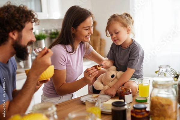 Obraz A family shares laughter and good times at home during breakfast. The parents help their daughter enjoy her meal, creating a warm atmosphere filled with love.