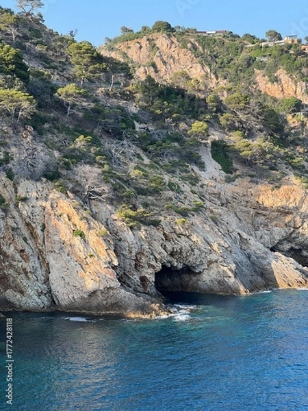 Obraz Dramatic rocky cliff with a natural cave opening and deep blue sea below
