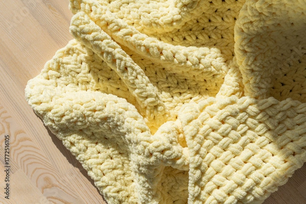 Fototapeta textured yellow knitted blanket draped on a wooden surface in soft light
