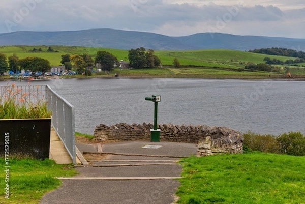 Obraz A scenic overlook includes a telescope at a lake, surrounded by green grass. Mountains form the background in Killington Lake - Kendal - Lake District - UK