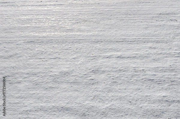 Fototapeta A textured, snow-covered surface showing subtle drifts and horizontal lines created by wind or light traffic, under bright natural light.
