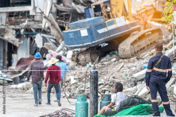 Fototapeta Worker controlling backhoe demolishing old buildings. Workers at demolition site with pile of rubble and bulldozer at Bangkok site.