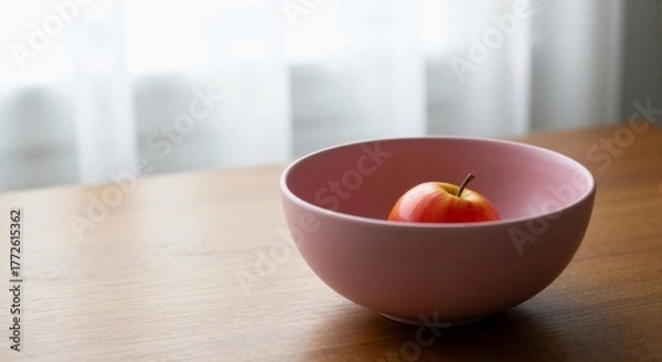 Fototapeta A red apple in a pink bowl on a wooden table – simplicity as luxury, an apple as a symbol, minimalist poetry, morning light.