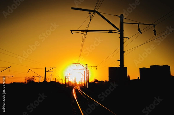 Fototapeta Railway - Railroad at sunset with sun, Rails and electric lines in yellow light