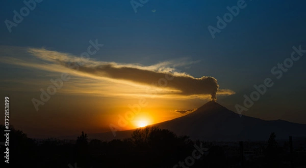 Fototapeta Stunning silhouette of Popocatépetl volcano erupting during a vibrant sunset. Fumarole and ash emerging under a dramatic sky in Mexico.