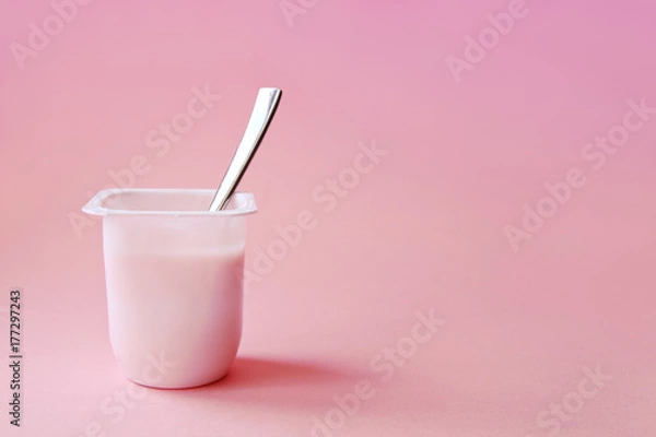 Fototapeta Delicious strawberry yogurt or pudding  in white plastic cup on pink background with copy space. Strawberry pink yoghurt with spoon in it. Minimal style.