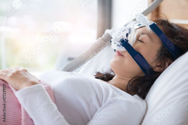 Obraz Kobieta i maska ​​cpap, koncepcja opieki zdrowotnej. Starsza kobieta używa maszyny cpap, aby przestać krztusić się i chrapać z powodu obturacyjnego bezdechu sennego z bokeh i porannym tłem.