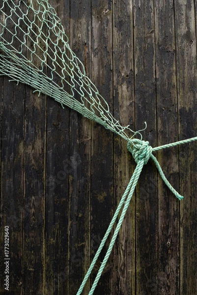Fototapeta A green fishing net resting on dark wooden planks, evoking a rustic and nautical atmosphere.