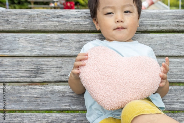 Obraz ハートのクッションを持ってベンチに座る男の子（2歳、日本人）