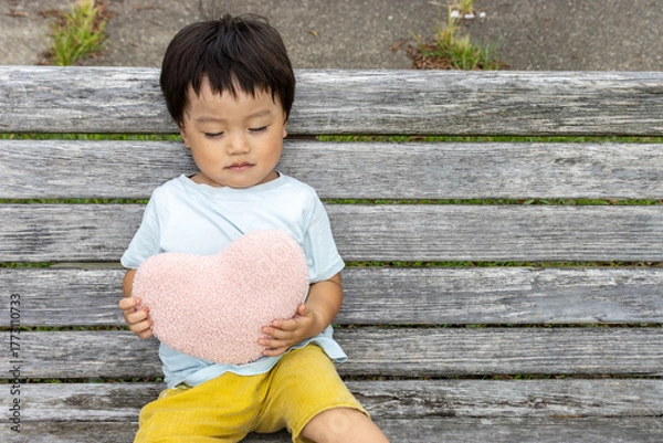 Obraz ハートのクッションを持ってベンチに座る男の子（2歳、日本人）