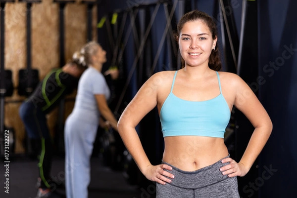 Fototapeta Smiling young woman fitness instructor welcoming to gym