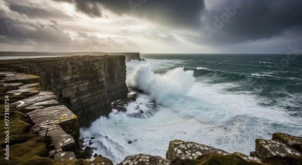 Fototapeta Powerful waves crash against majestic coastal cliffs under a dramatic, stormy sky, showcasing the raw beauty of a rugged coastline with sunlight breaking through clouds.