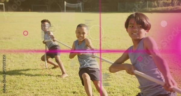 Fototapeta Pulling rope, three boys in grey sleeveless shirts competing on grassy field, with soccer goalposts