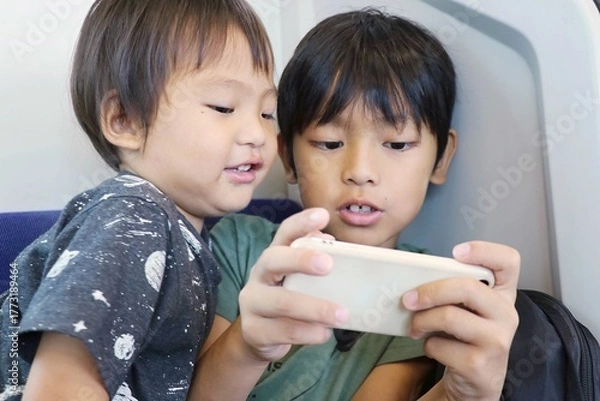 Obraz 電車内でスマートフォンを閲覧している子供達　アジアの日本人の兄弟