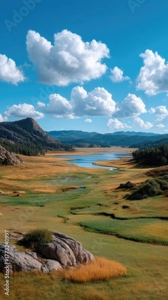 Fototapeta Vast Open Field Under a Dramatic Blue Sky with Puffy White Clouds and Distant Rocky Hills Reflected in a Serene Lake