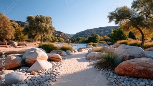 Fototapeta Sunlit Rocky Path Meandering Through a Serene Valley with Distant River and Lush Green Trees Under a Clear Blue Sky