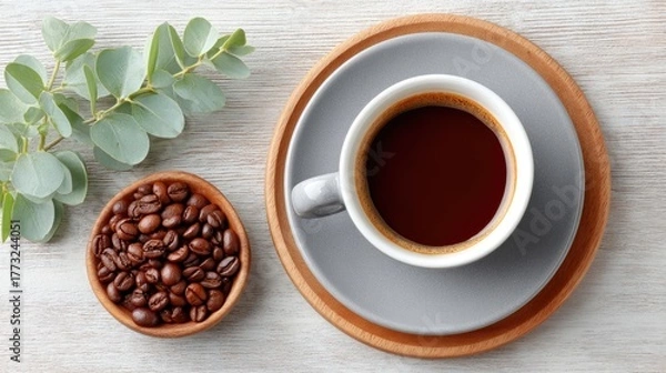 Fototapeta Top View Flat Lay of Roasted Coffee Beans in Wooden Bowl Next to Grey Cup of Black Coffee on White Wooden Table with Eucalyptus Sprig