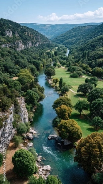 Fototapeta Wide Verdant Valley With A Flowing Blue River On A Sunny Day With Rocky Cliffs And Lush Green Trees