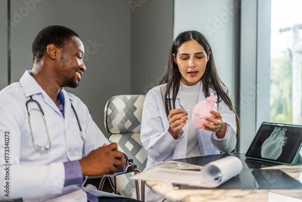 Fototapeta Two cardiologists engage in a detailed discussion on heart disease treatment, using an anatomical model to illustrate their points while consulting with a medical intern in a clinic, share knowledge
