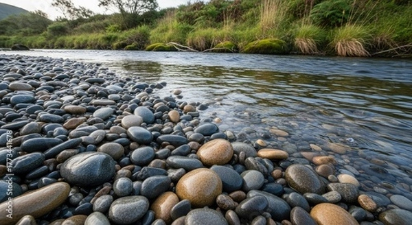 Obraz River flowing over rocks with vegetation on the bank in the distance