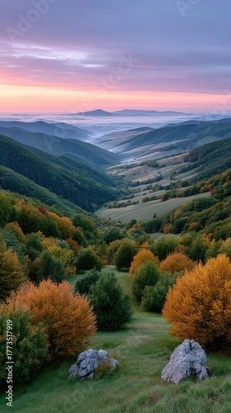 Fototapeta Serene mountain valley at dawn with mist rising revealing rolling hills and distant plateau under a pastel sky with soft pink and purple hues and vibrant autumn foliage in the foreground