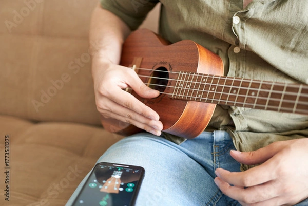 Fototapeta man playing ukulele with smart phone on sofa at home