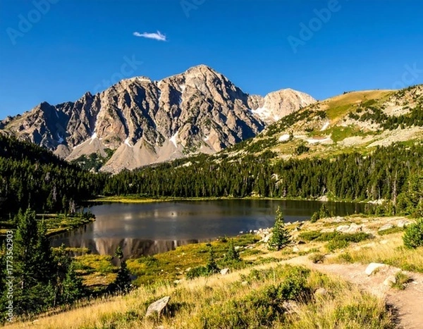 Obraz Sunny mountain peak looms over a calm lake with verdant trees