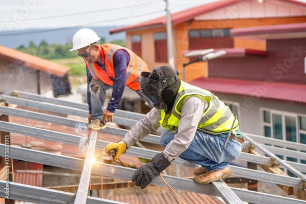 Fototapeta Construction Workers Engaged in Metal Roof Installation with Safety Gear on a Sunny Day at a Building Site in Focused Action