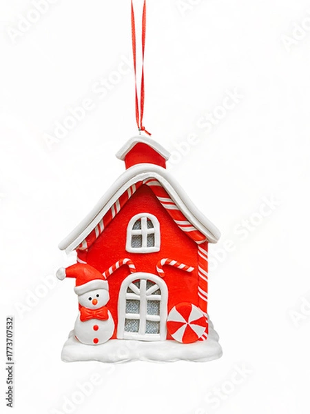 Obraz A charming red ceramic Christmas ornament shaped like a candy-cane-roofed house, featuring a snowman. Hanging on a ribbon, perfectly isolated on white for holiday design