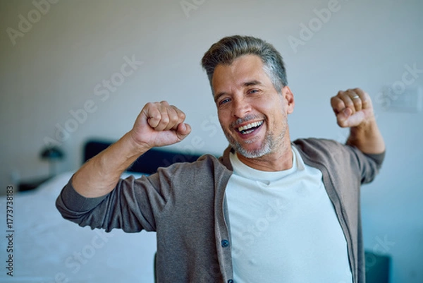 Fototapeta Middle-aged man stretching in bed with a bright smile, feeling energetic, triumphant and optimistic about a fresh morning