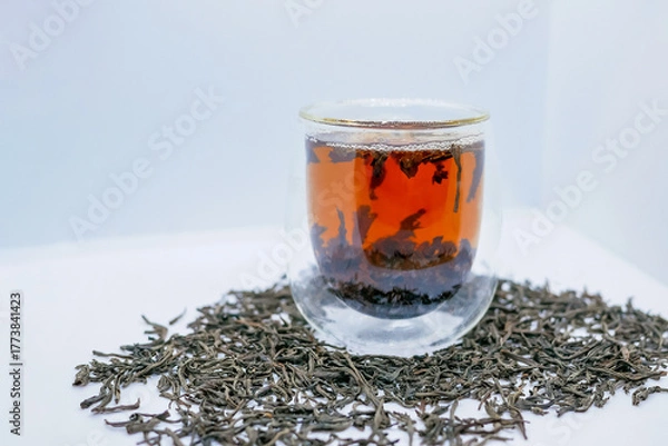 Fototapeta Glass Cup of Black Tea and Loose Leaves on White Background