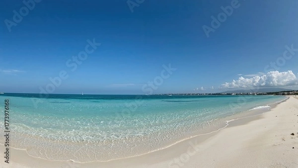Fototapeta Tropical beach with clear blue water and white sand under a bright sky. Coastal scenery with calm waves and distant horizon.
