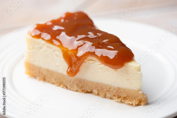 Fototapeta Cheesecake slice with caramel sauce topping on a white dessert plate, closeup view