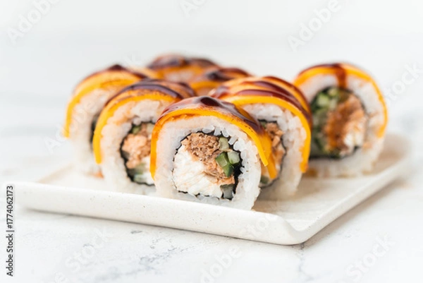 Fototapeta Sushi roll with salmon,  avocado and tuna. Sushi set served on the white plate next to red ginger with wooden sticks on the white background